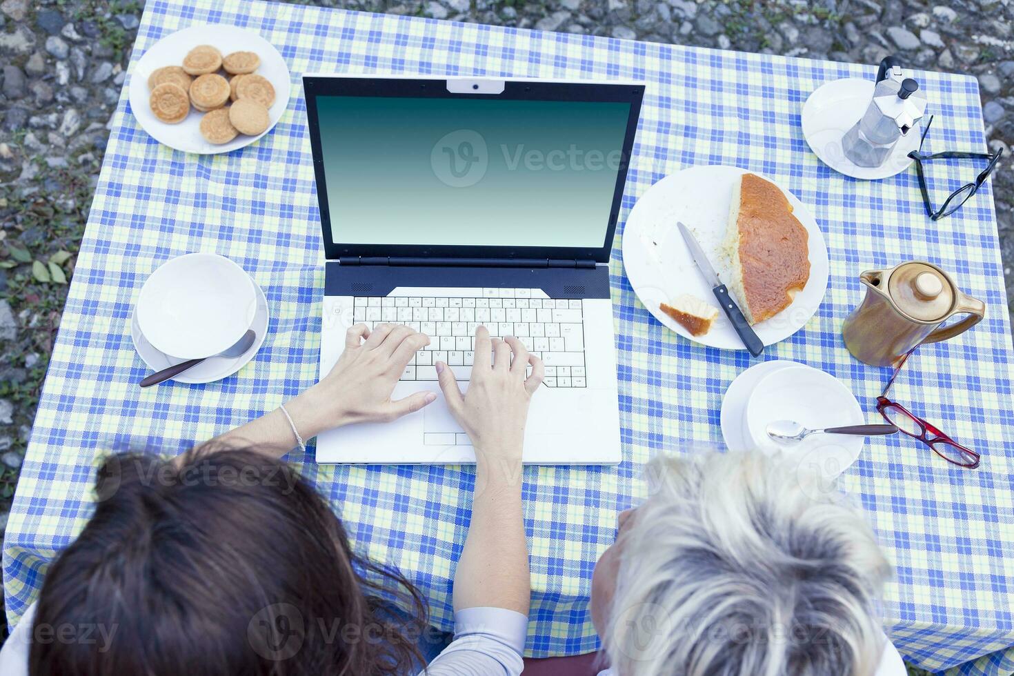 pretty mom and daughter consult the laptop while having breakfast outdoors photo