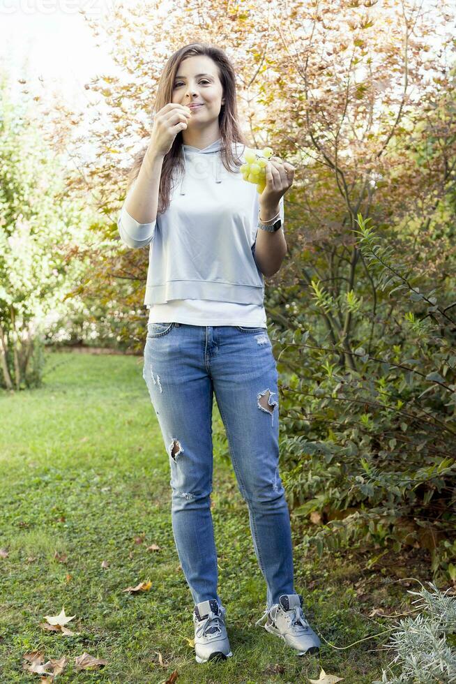 joven hermosa niña sentado debajo un árbol comiendo uvas foto