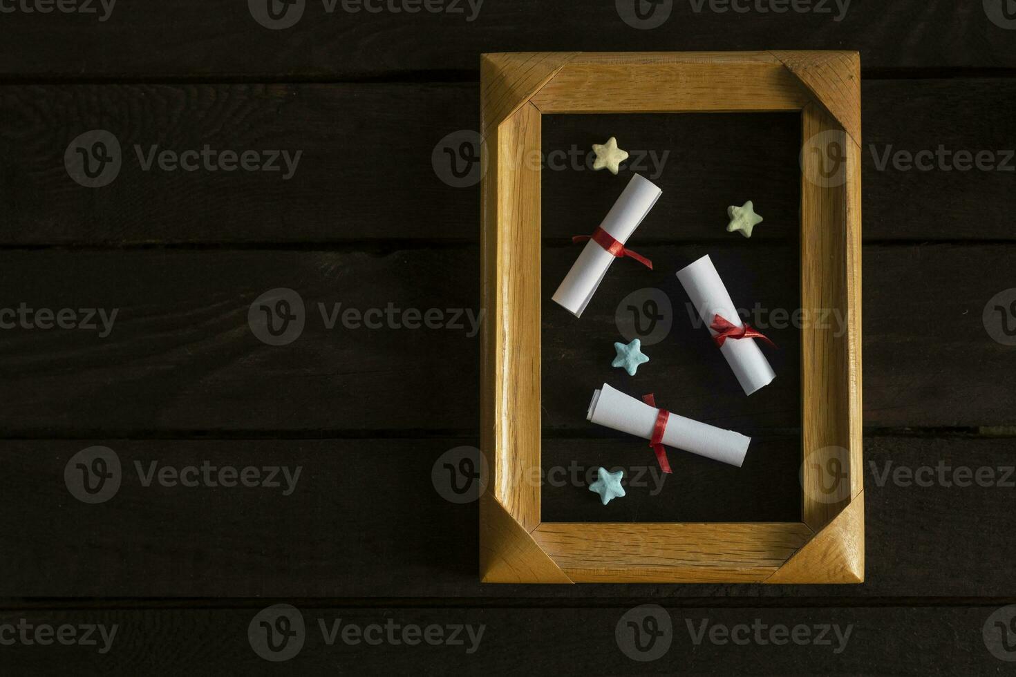 Flat lay romantic background. Giftbox, rolled wish papers, and wooden frame with paper hearts on dark wood board. photo