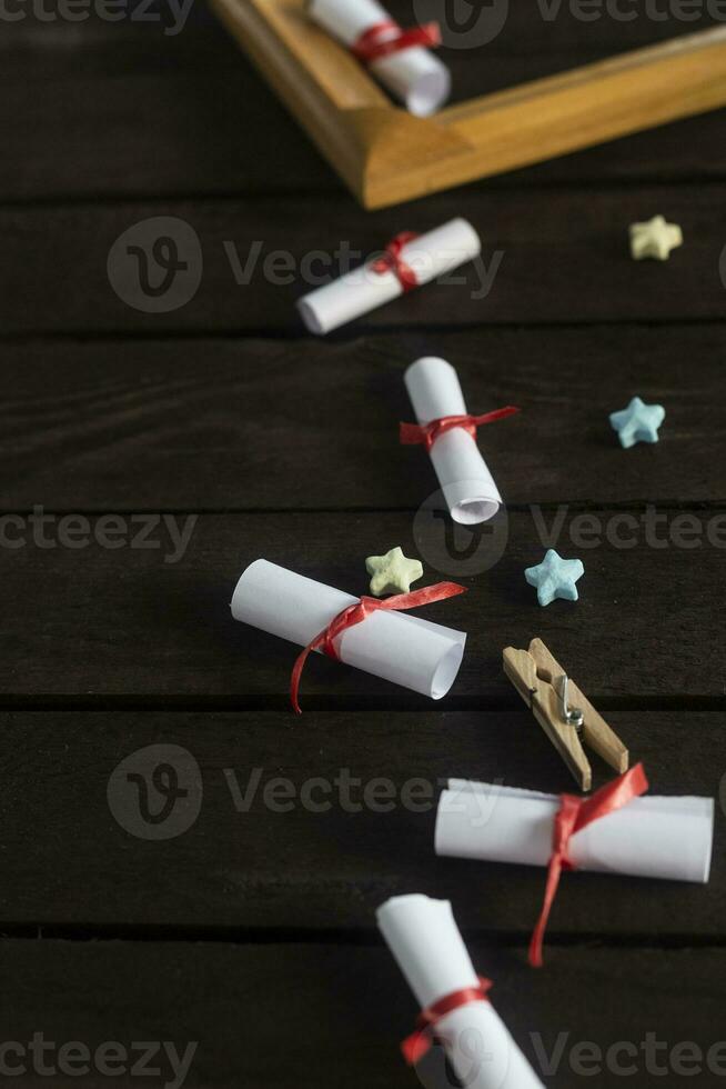 Flat lay romantic background. Giftbox, rolled wish papers, and wooden frame with paper hearts on dark wood board. photo