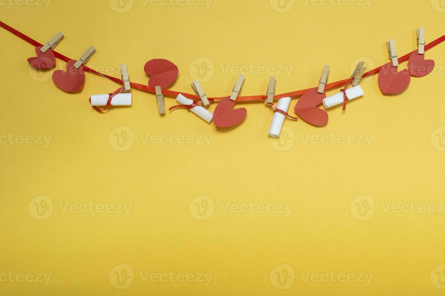 Red hearts and rolled wish papers on rope with clothespins on yellow. Place for text, copy space photo