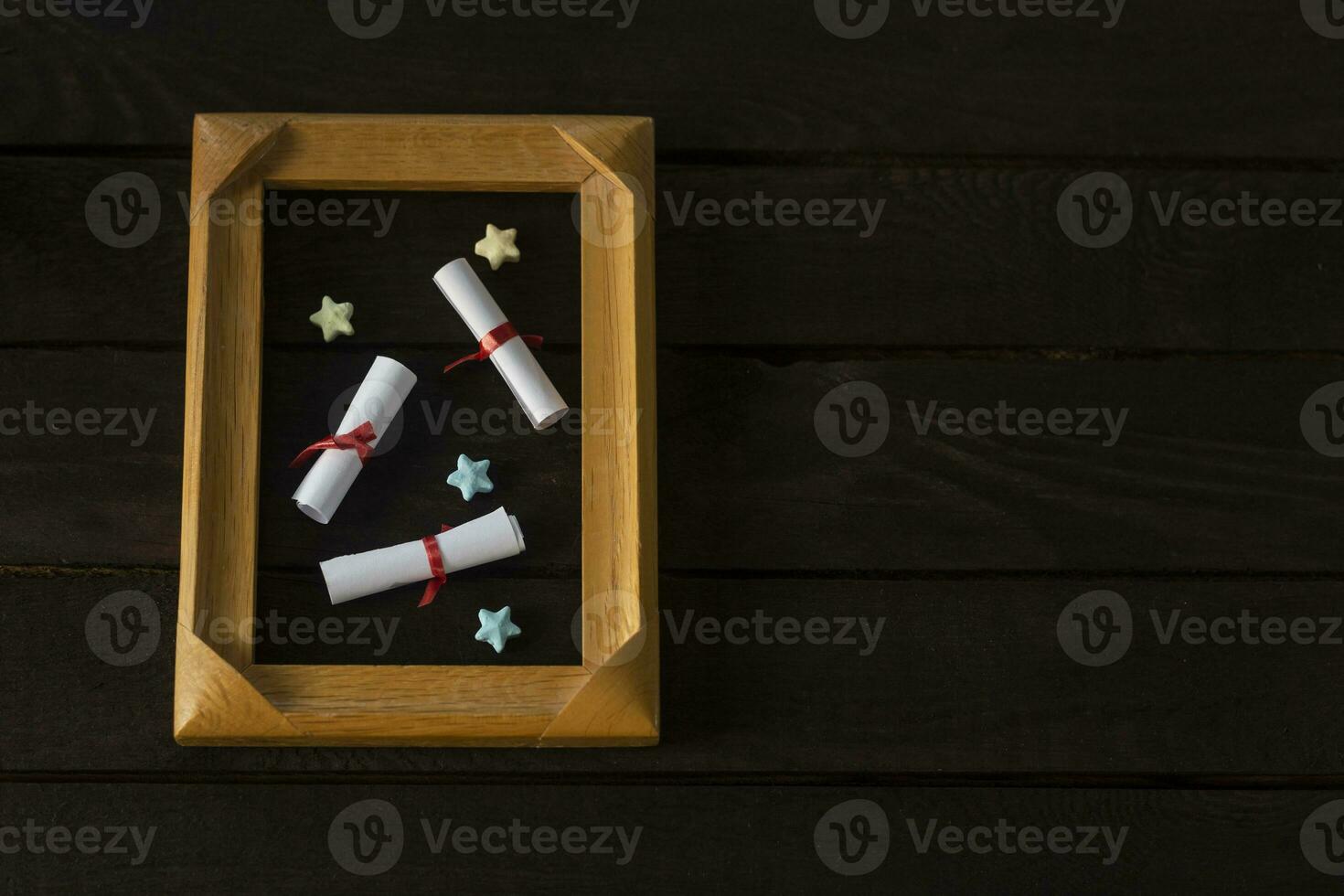 Flat lay romantic background. Giftbox, rolled wish papers, and wooden frame with paper hearts on dark wood board. photo