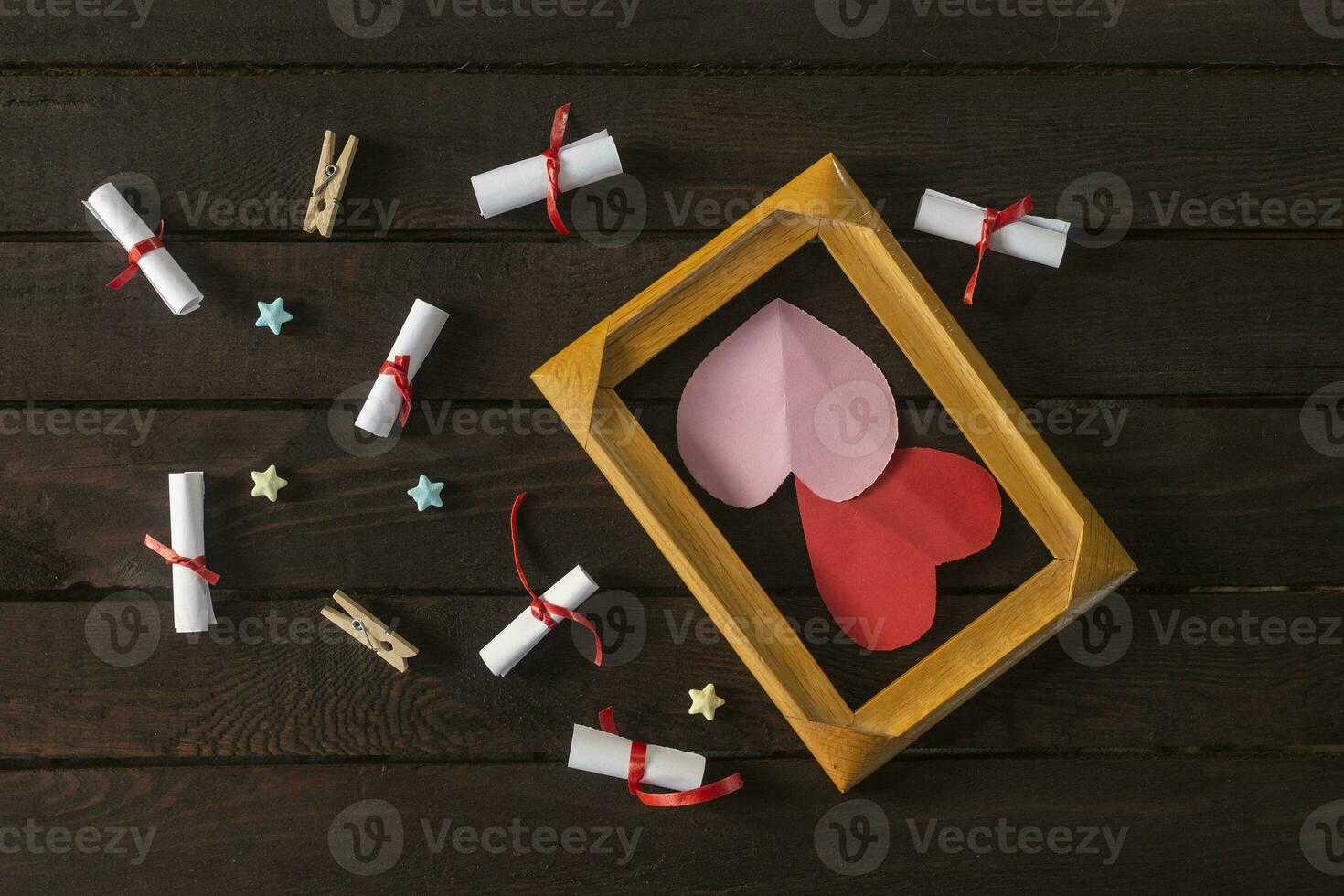 Flat lay romantic background. Giftbox, rolled wish papers, and wooden frame with paper hearts on dark wood board. photo