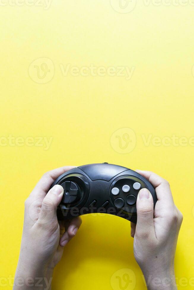 Vertical view to hands holding black gamepad and playing video game against yellow photo