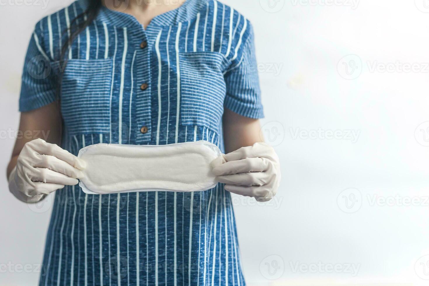 Female's hygiene products. Woman in medical gloves holding sanitary pads against white background. Period days concept showing feminine menstrual cycle. photo