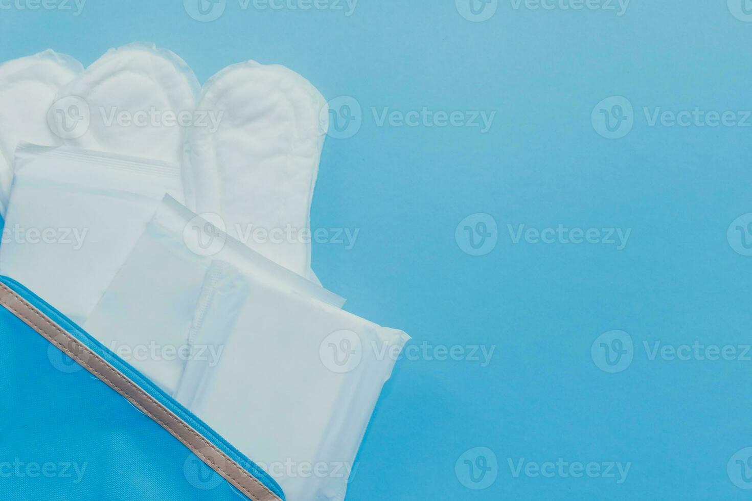 Female's hygiene products. Women's bag and sanitary pads on blue background photo