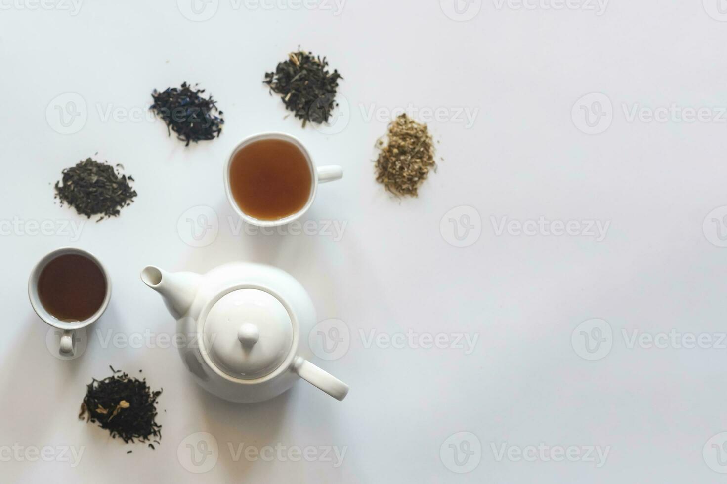 Tea set with white ceramic tea pot and other tea ingredients on the white. Flat lay view of various dried teas and teapot. View from above. Space for your text photo