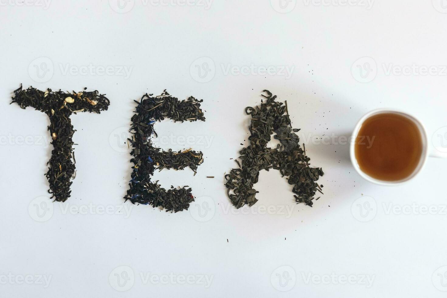 The word tea made with dry tea leafs and a cup of black tea photo