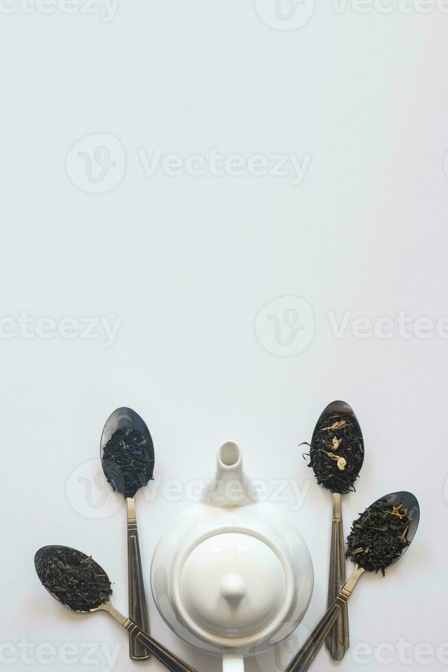 White ceramic tea pot and various dried teas on the white background. Flat lay view. Space for your text photo