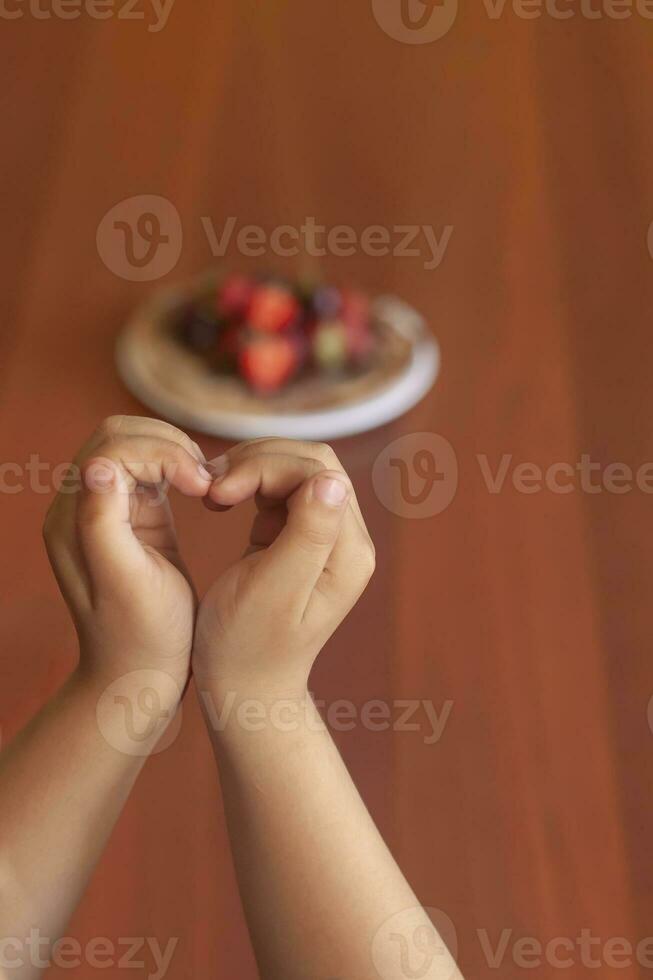 un joven mujer participación un plato de Delgado panqueques con fresas y chocolate crema. hembra comiendo panqueques con Fresco fresas foto