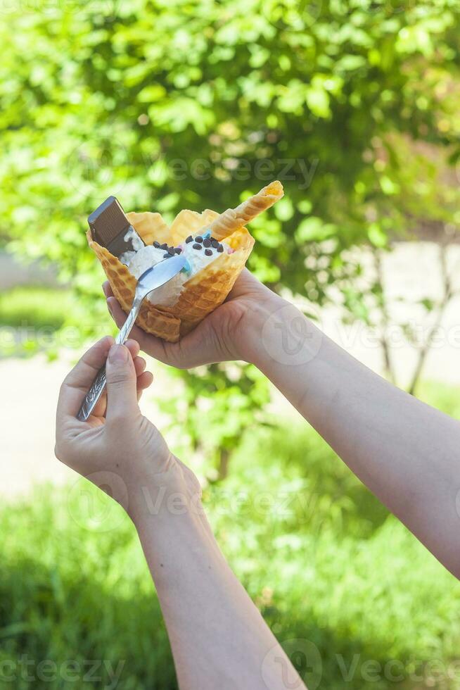 Young woman holding delicious ice cream with waffle during a picnic at nature. Summer food concept. Young adult eating yummy ice cream with a stick on a bright summer day. photo