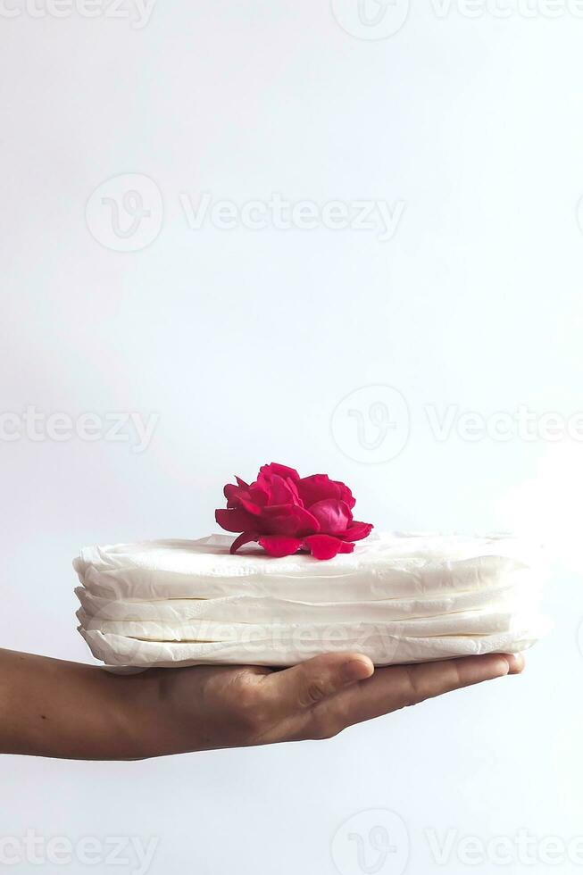 Woman's hand holding a stack of sanitary napkins with red rose on. Against white background. Period days concept showing feminine menstrual cycle. photo