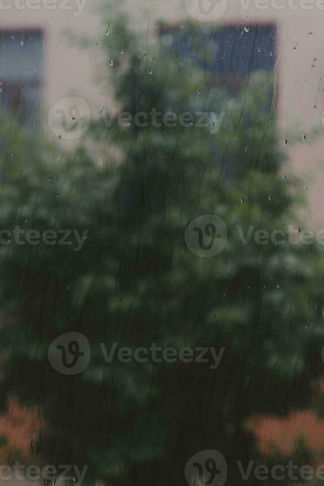 View to raining weather through the home window. Raindrops on the window glass. Heavy raining outdoors. Spring rain season photo