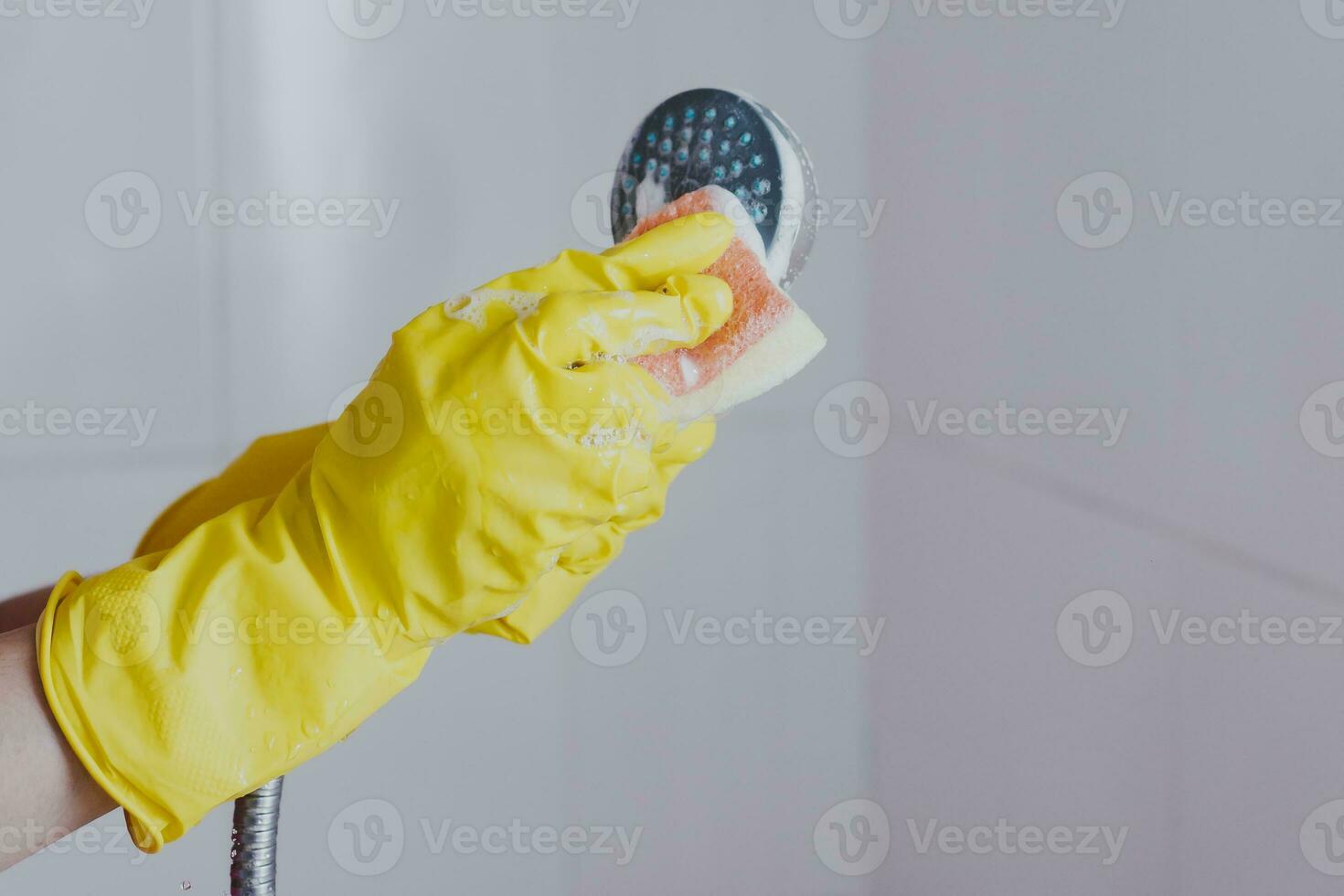 Woman in rubber gloves cleaning the shower head. Housemaid washing metallic head of the shower. Housewife cleaning up in the bathroom photo