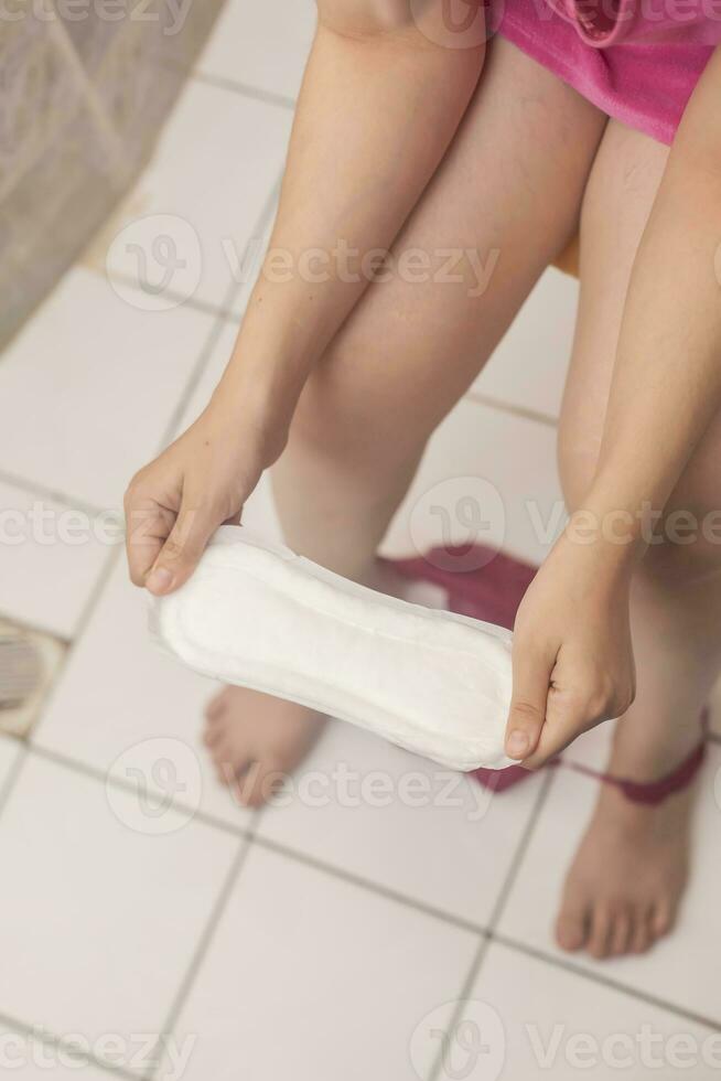 Woman in a toilet with a sanitary napkin. Young girl holds a sanitary pad while sitting in a toilet photo