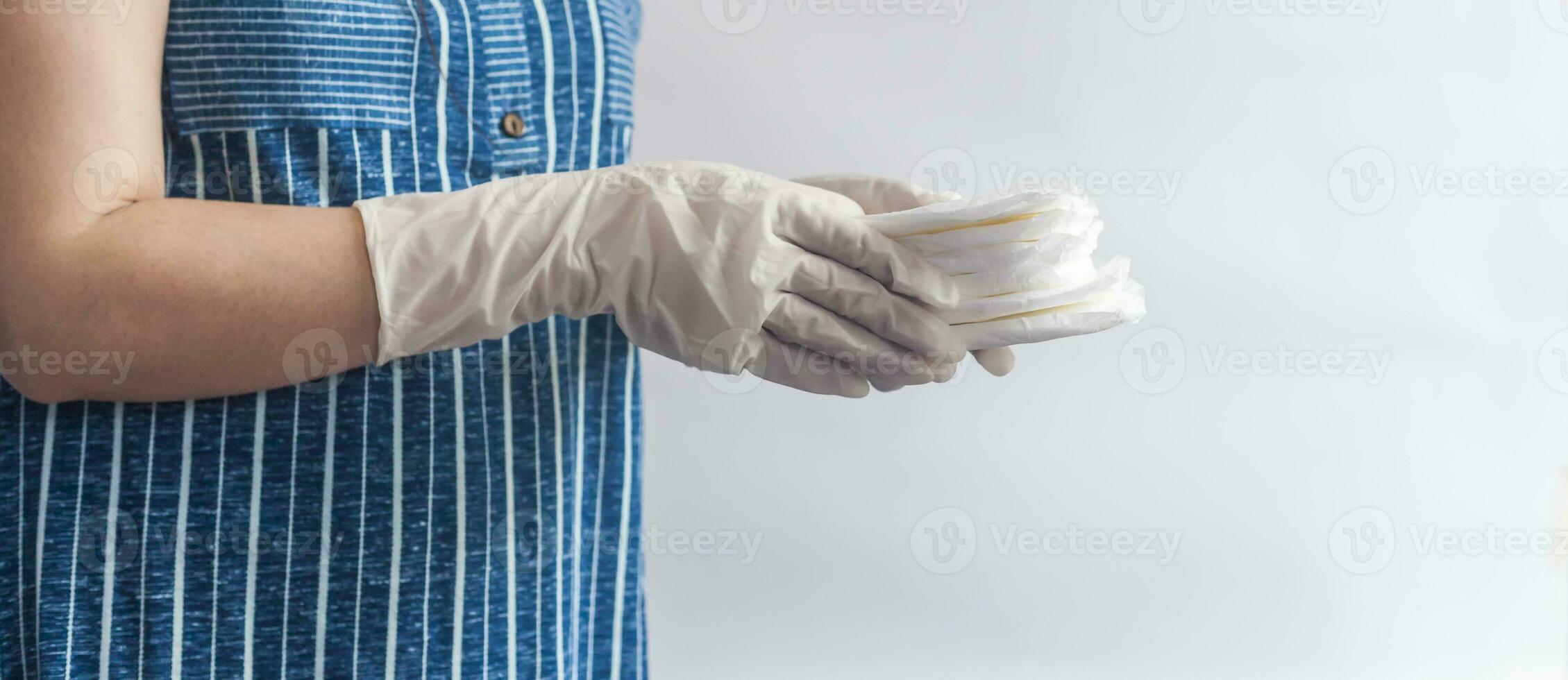 Female's hygiene products. Woman in medical gloves holding a stack of sanitary napkins against white background. Period days concept showing feminine menstrual cycle. photo