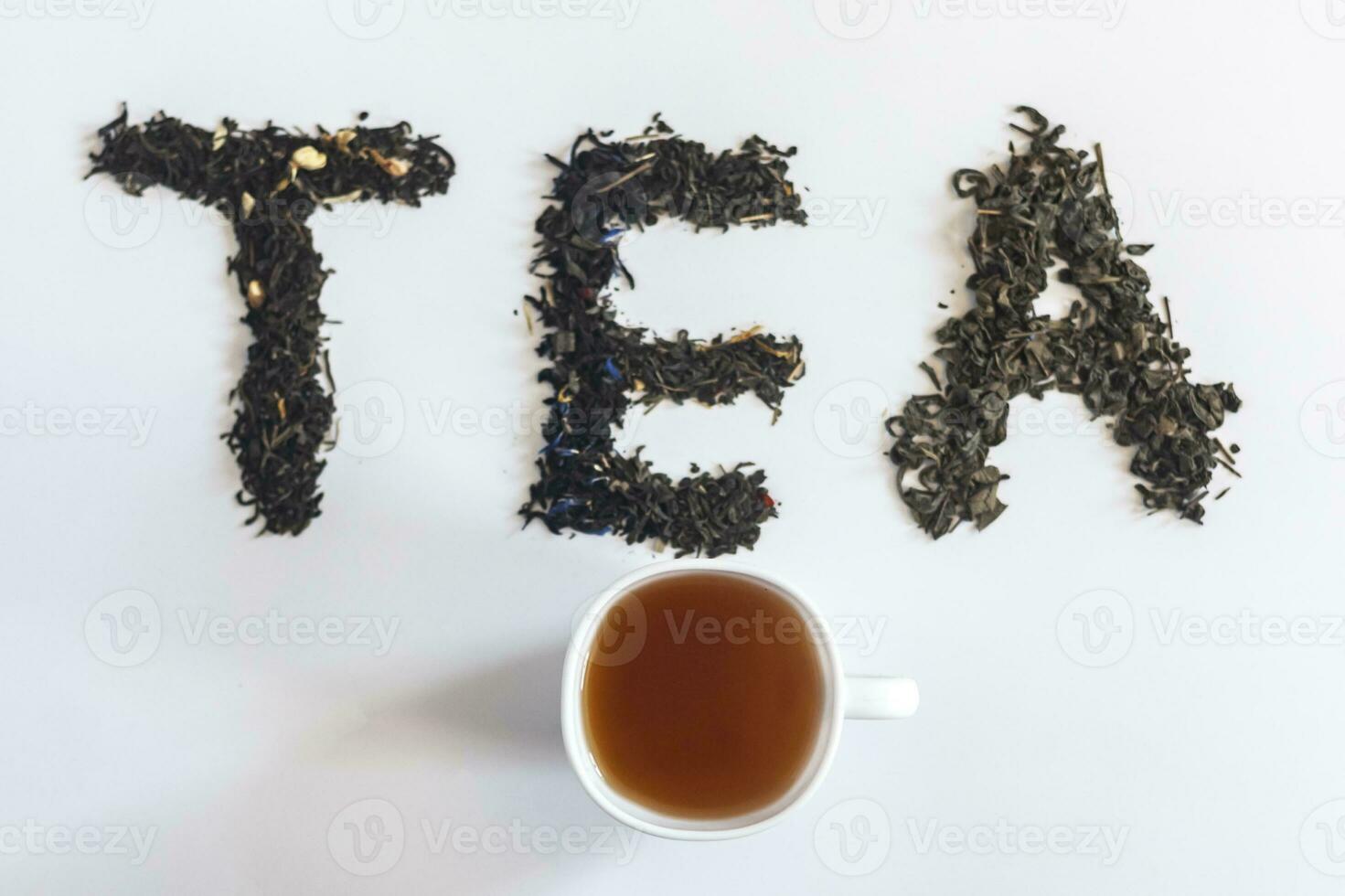 The word tea made with dry tea leafs and a cup of black tea photo