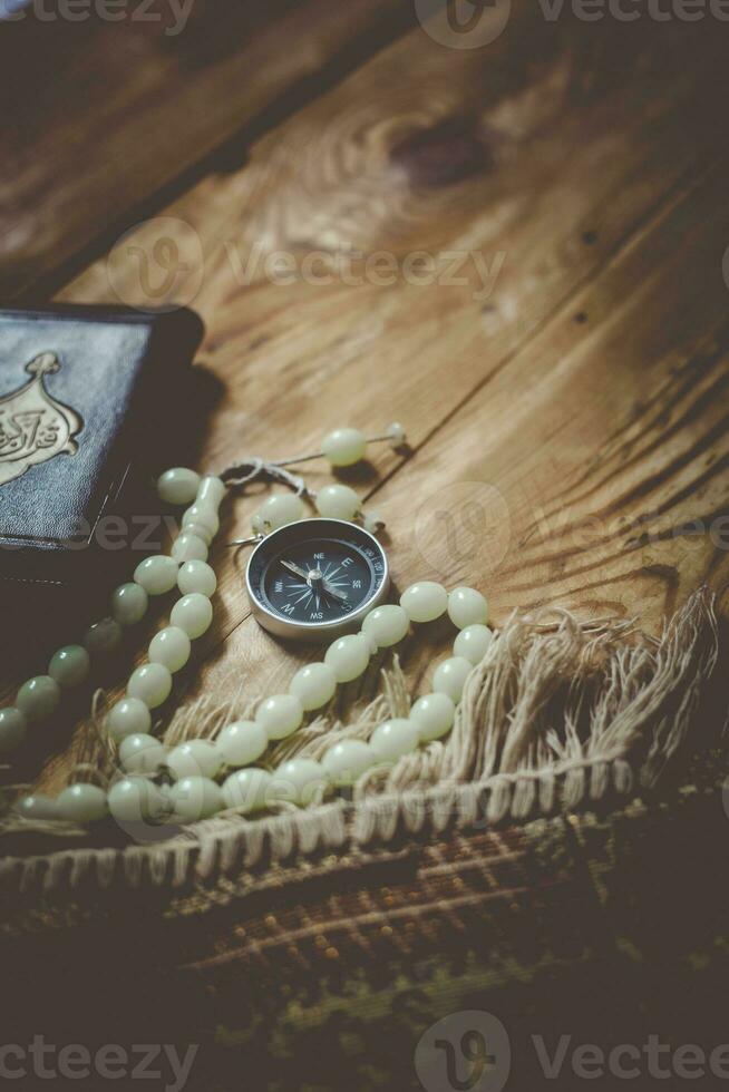 Traditional muslim prayer set bundle. Praying carpet, rosary beads, little version of the Holy Quran and qibla compass on wooden background. Free Space photo
