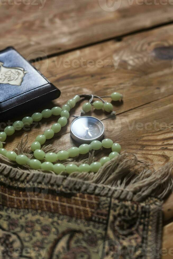 Traditional muslim prayer set bundle. Praying carpet, rosary beads, little version of the Holy Quran and qibla compass on wooden background. Free Space photo