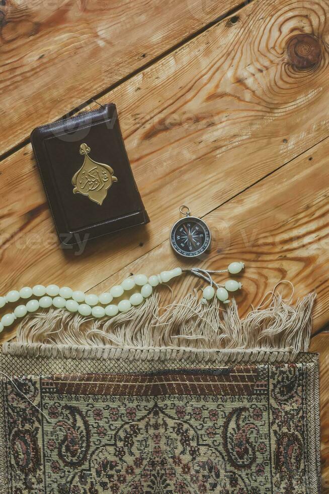 Traditional muslim prayer set bundle. Praying carpet, rosary beads, little version of the Holy Quran and qibla compass on wooden background. Free Space photo