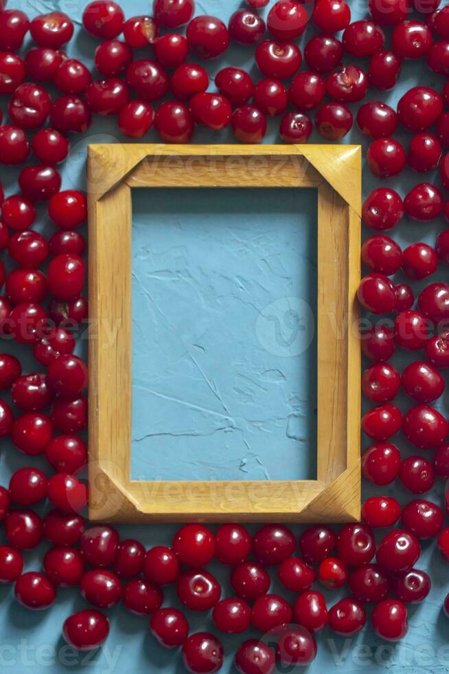 de madera marco con Copiar espacio y maduro cerezas en azul antecedentes. bayas y frutas alrededor el vacío madera marco foto