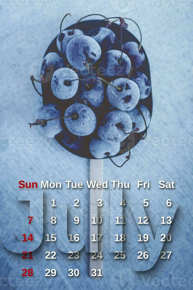 July calendar. Stack of frozen sweet cherries with July month calendar. Summer photo
