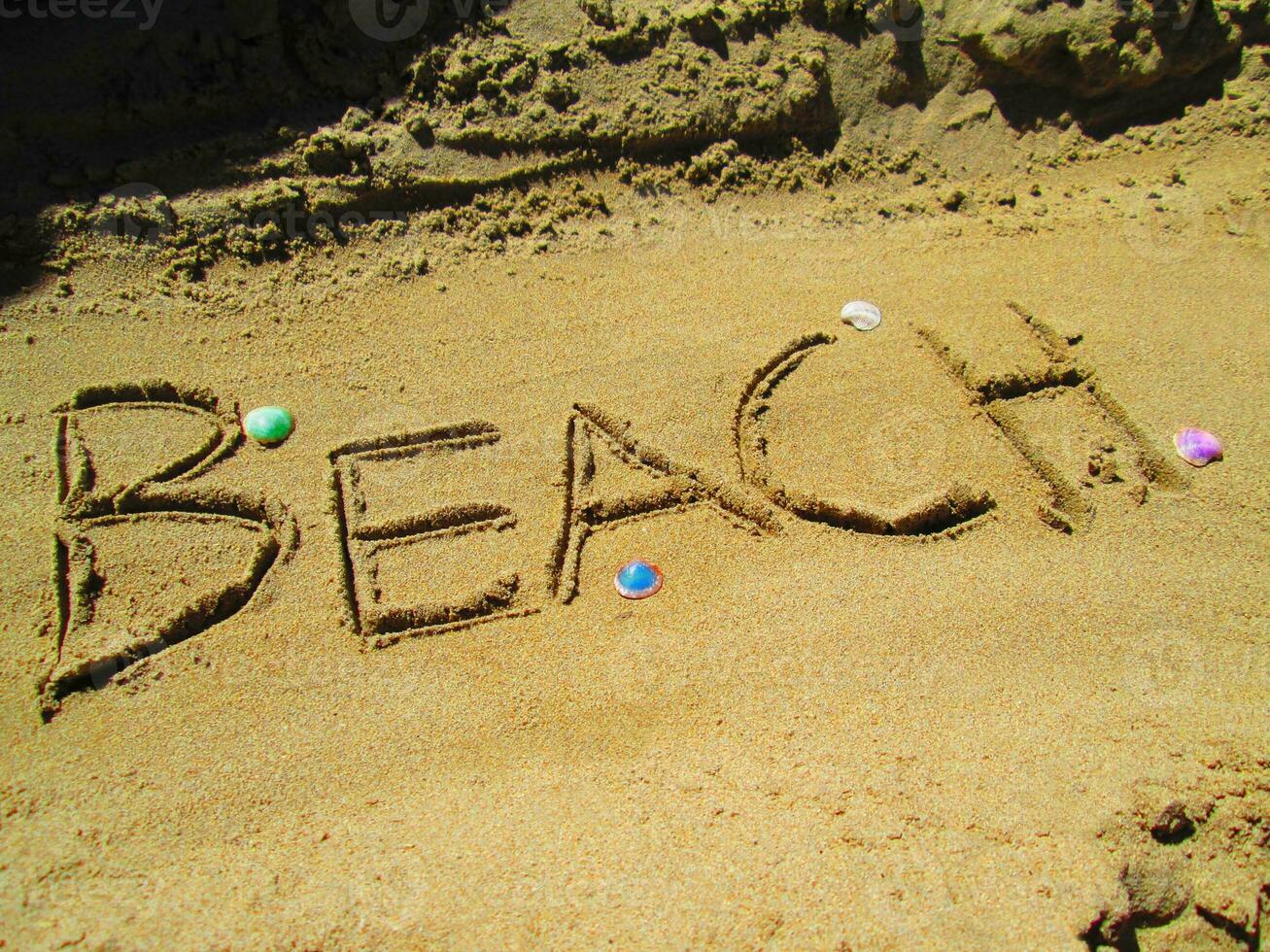 Beach spelled in a sand - colorful seashells photo