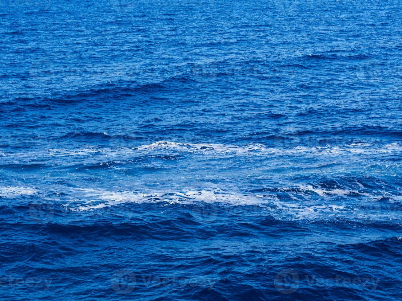 Straight boat wake left on the deep blue surface of the sea photo