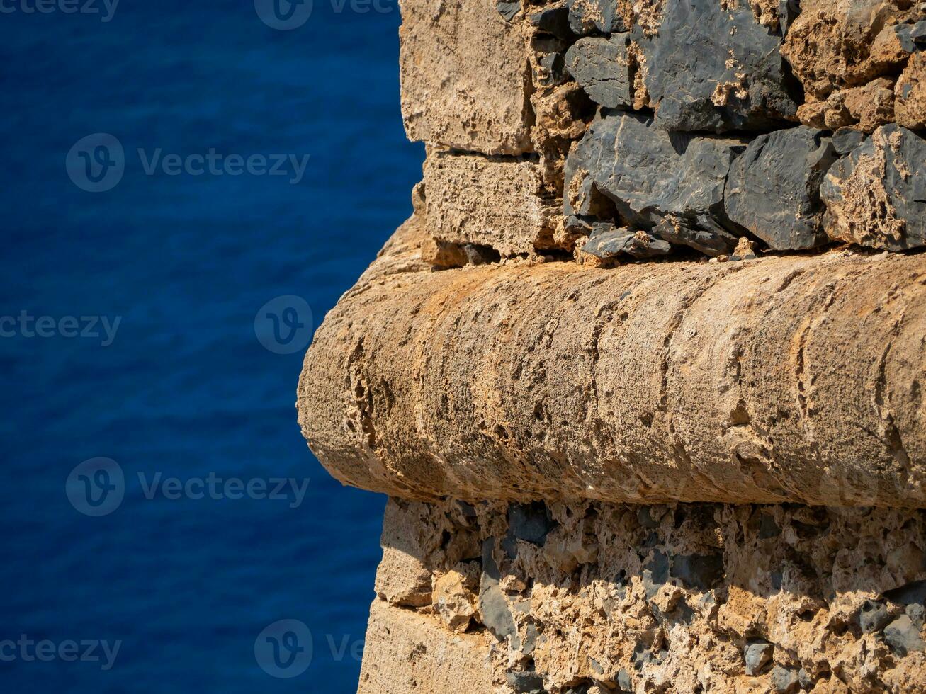 Decorative detail in the ancient fort wall in Crete, Greece - blue sea in the background photo