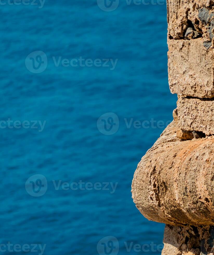 Orange stone wall of medieval fortress - blue sea in the background photo