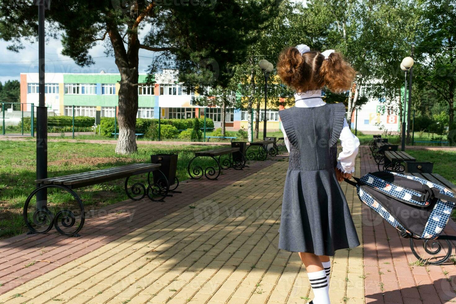 Pupil with backpack and in a school uniform in school yard back to the frame. Back to school, September 1. A happy student. Primary education, elementary class. Road to life, to knowledge photo