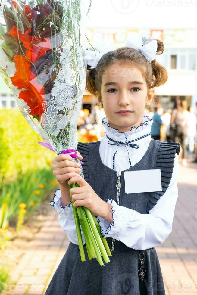 Portrait of a girl student of the 1st grade school with white bows and flowers in a dress unifor with badge mock up. Back to school, September 1, First - grade. Primary education, elementary class. photo