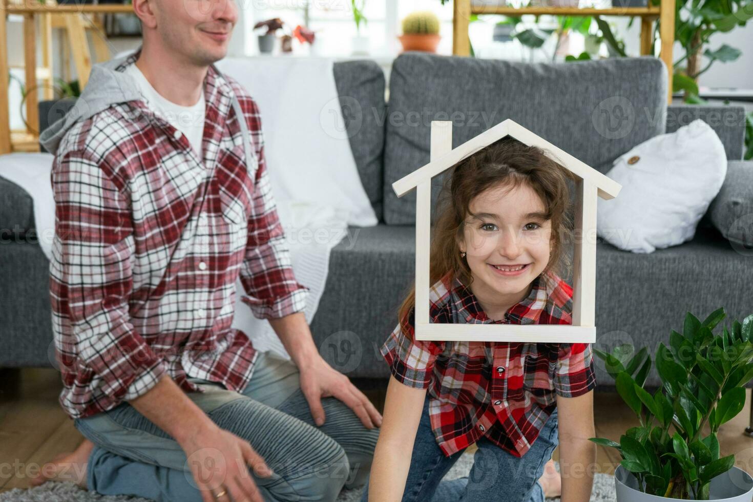 Incomplete family dad and daughter are enjoying new home, sitting on sofa. Mortgage, insurance and protection, buying and moving into your own home, green house with potted plant photo