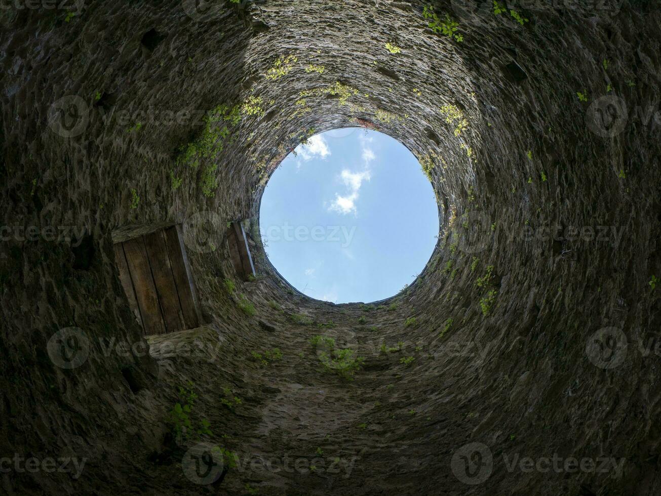 Stone well hole, old construction from inside, brick walls and blue sky background, fall down in the well concept photo