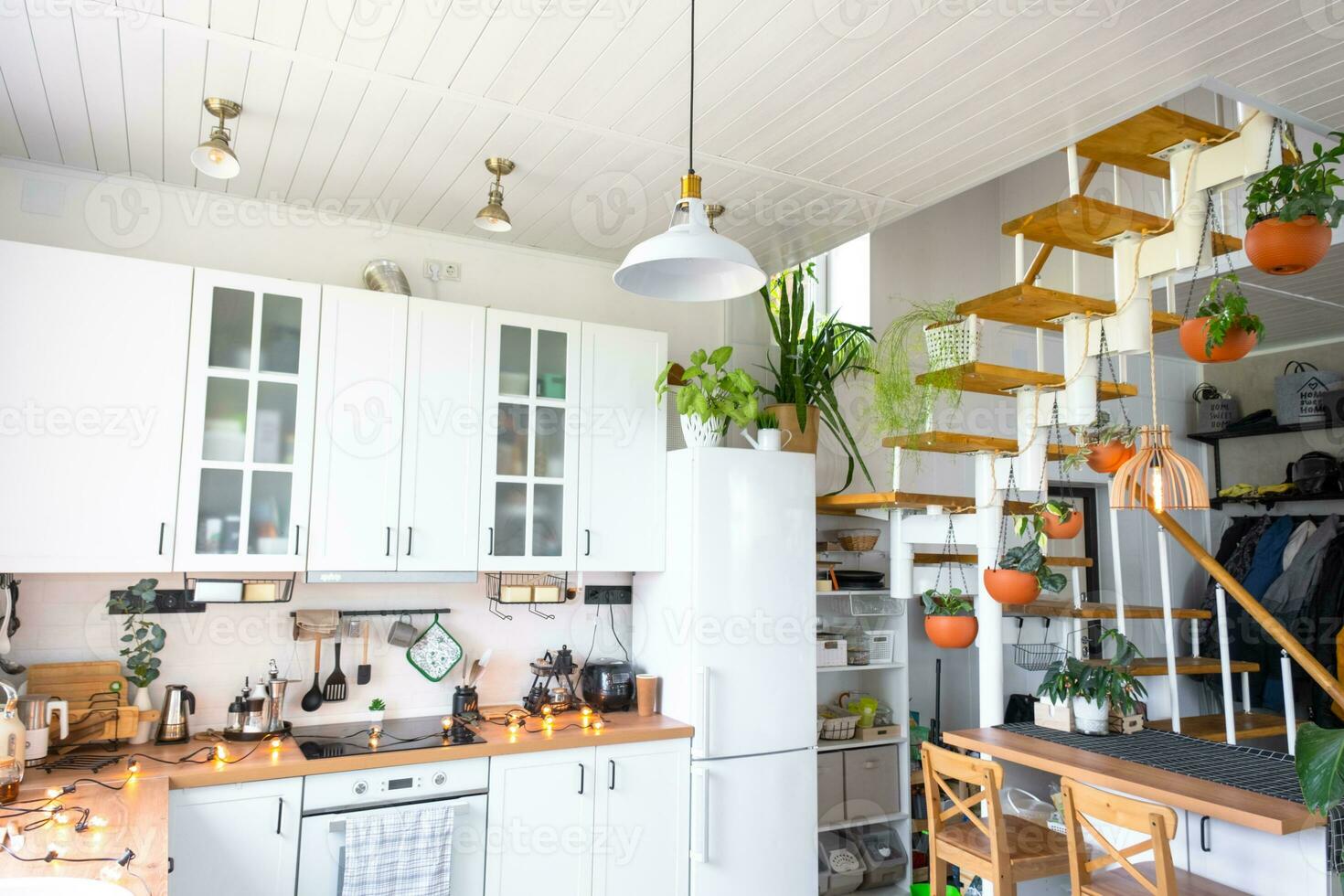 The general plan of a light white modern rustic kitchen with a modular metal staircase decorated with potted plants. Interior of a house with homeplants photo