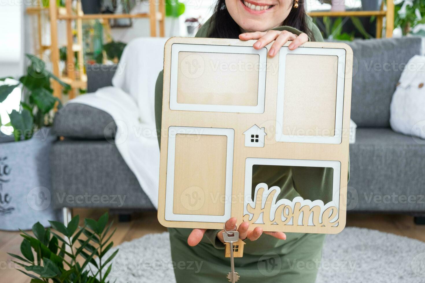 Happy woman in house holds in hands photo frame with figure at home template and key in interior. Dream house project, real estate purchase, insurance, mortgage, rent, reservation