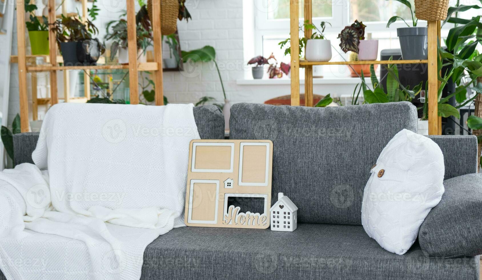 Key to home with keychain and mock up frame miniature of house on gray sofa in white interior with potted plants. Design, project, moving to new house, mortgage, rent and purchase real estate photo