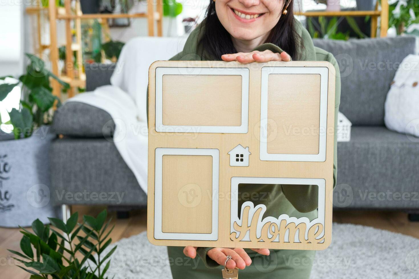 Happy woman in house holds in hands photo frame with figure at home template and key in interior. Dream house project, real estate purchase, insurance, mortgage, rent, reservation