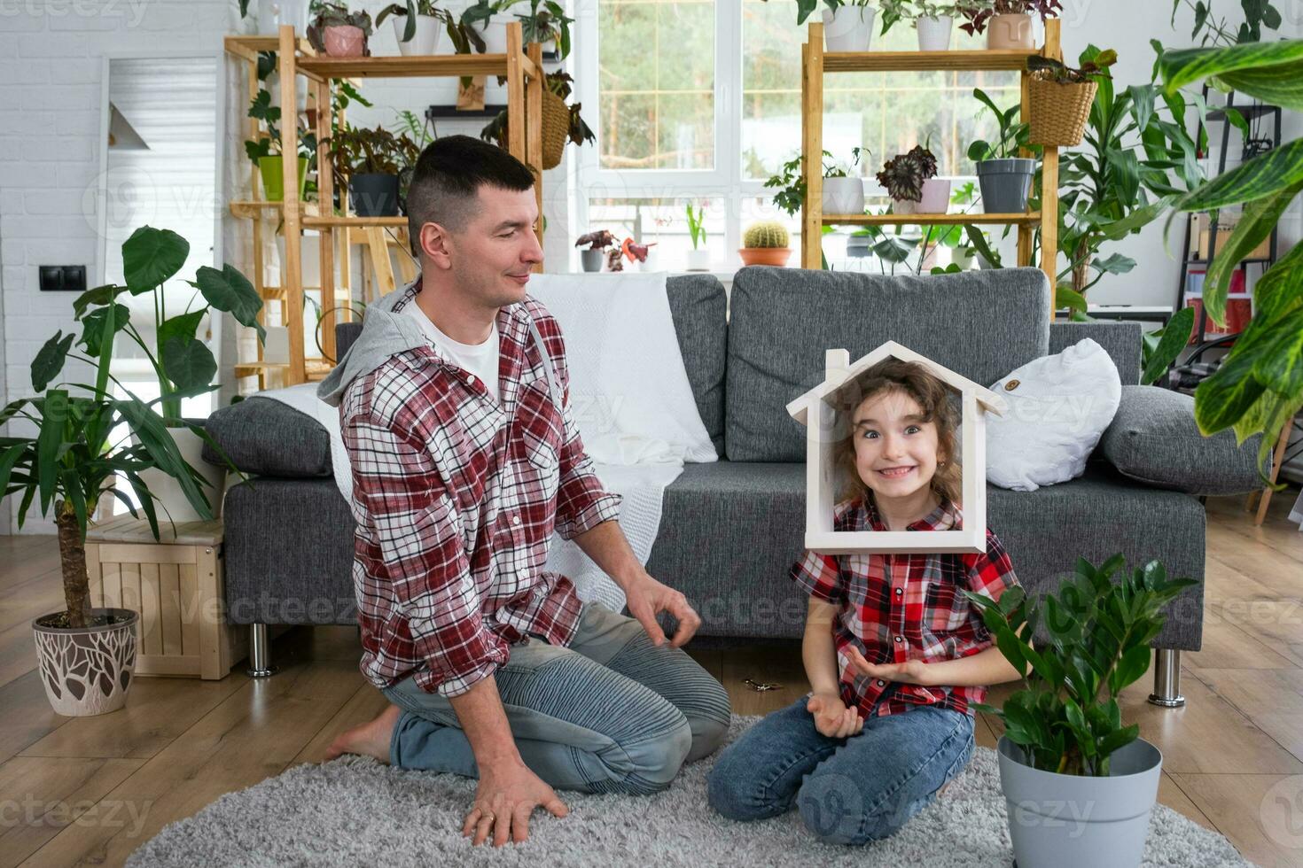 Incomplete family dad and daughter are enjoying new home, sitting on sofa. Mortgage, insurance and protection, buying and moving into your own home, green house with potted plant photo