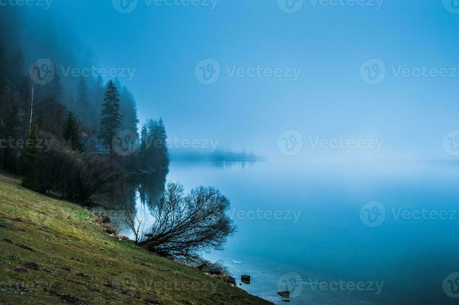 Foggy morning on the border of calm lake in Austrian Alps photo