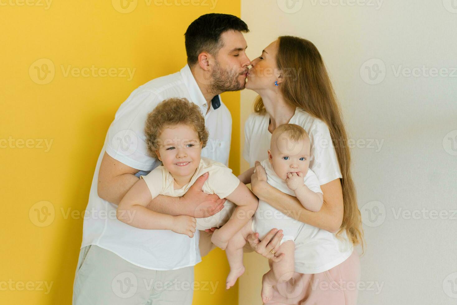 Young parents kiss while holding their sons' children in their arms. Happy family on a white yellow background photo