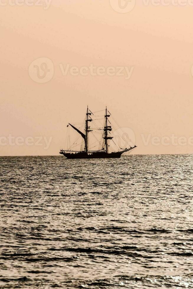 a tall ship in the ocean at sunset photo