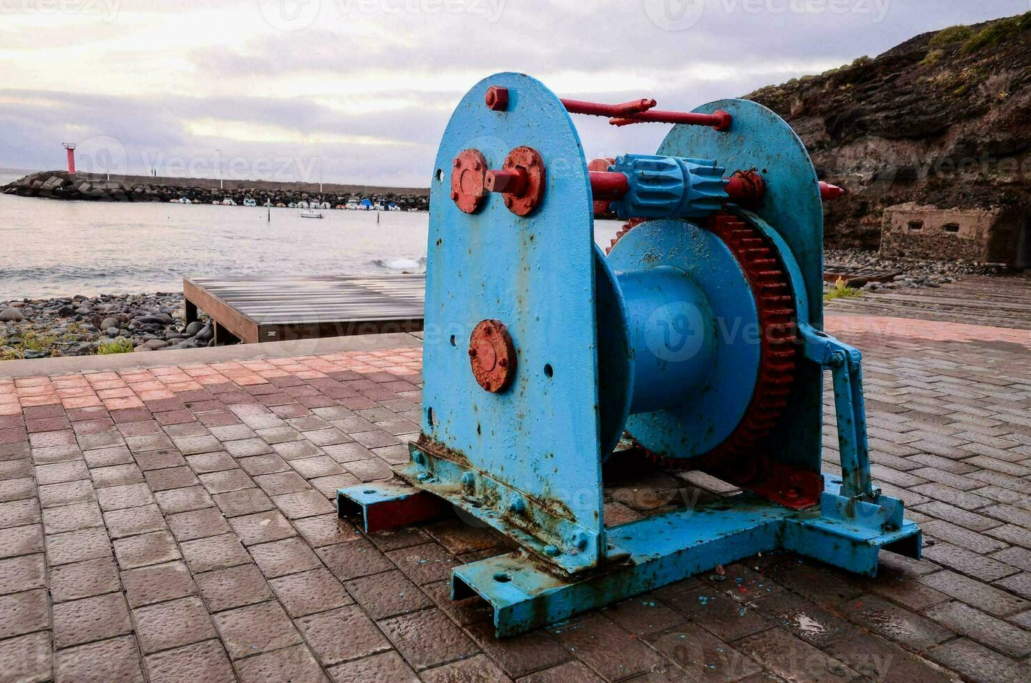 a blue and red machine sitting on the ground near the ocean photo