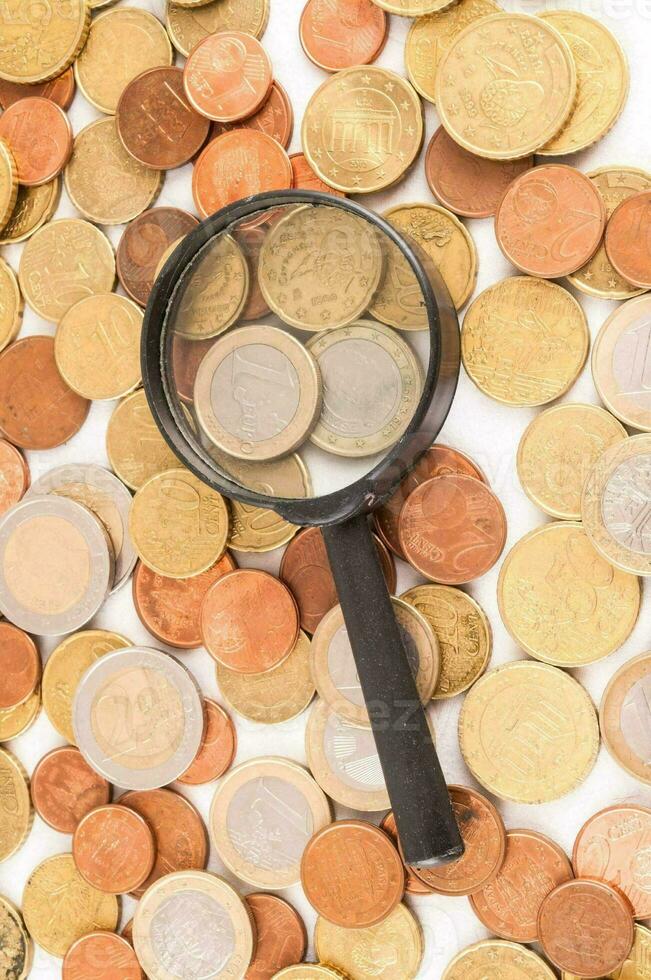 Magnifying glass with gold bar pile of gold coins under it