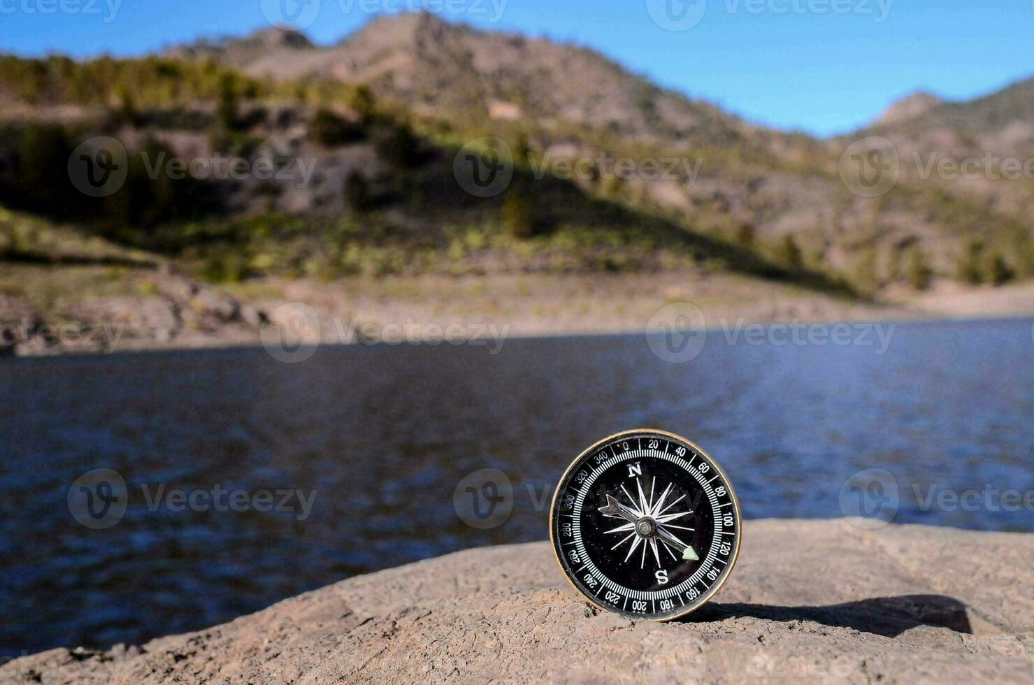 a compass on a rock near a lake photo