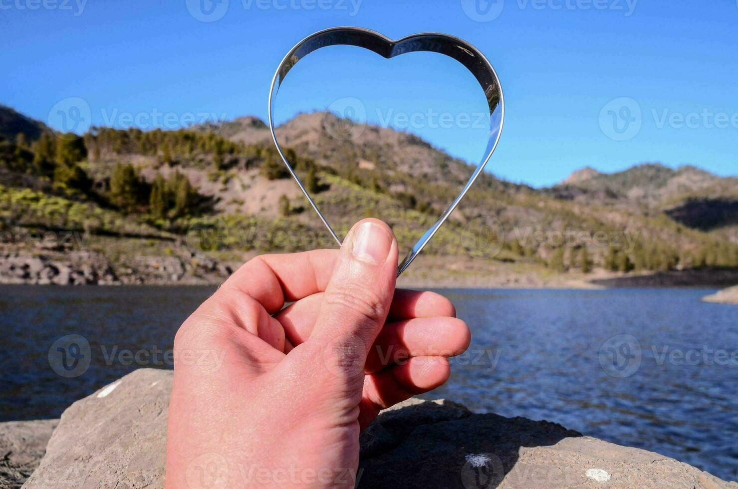 a person holding a heart shaped object in front of a lake photo