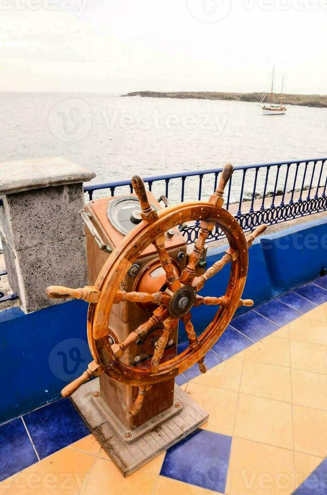 a wooden steering wheel on a dock near the ocean photo