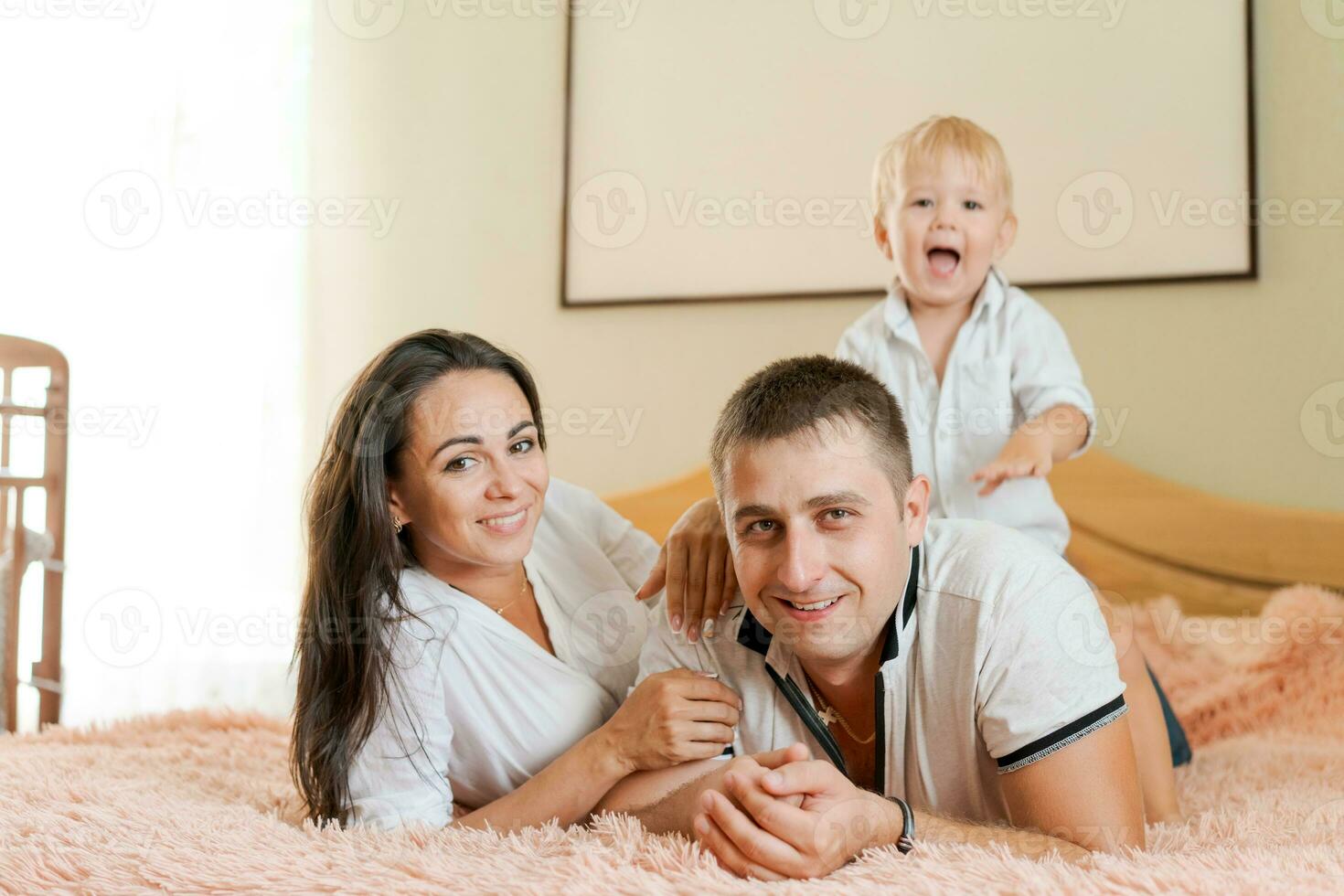 contento familia acostado en el cama y abrazando, mamá papá y pequeño hijo foto