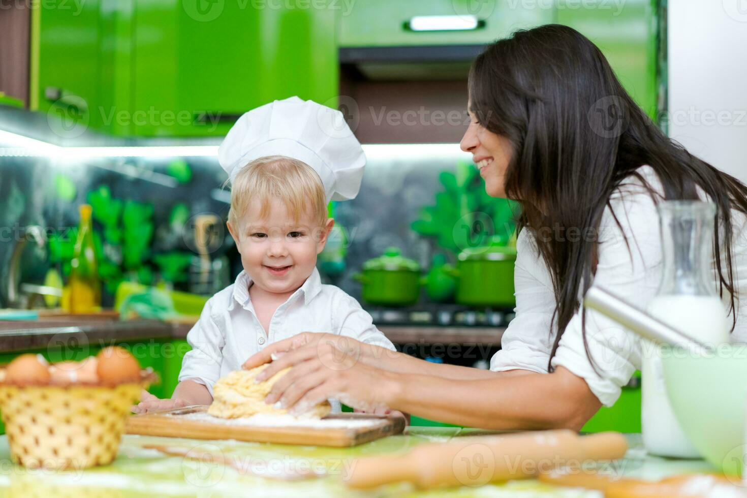 happy family mother and little son preparing dough in kitchen at table. products for dough are on table photo