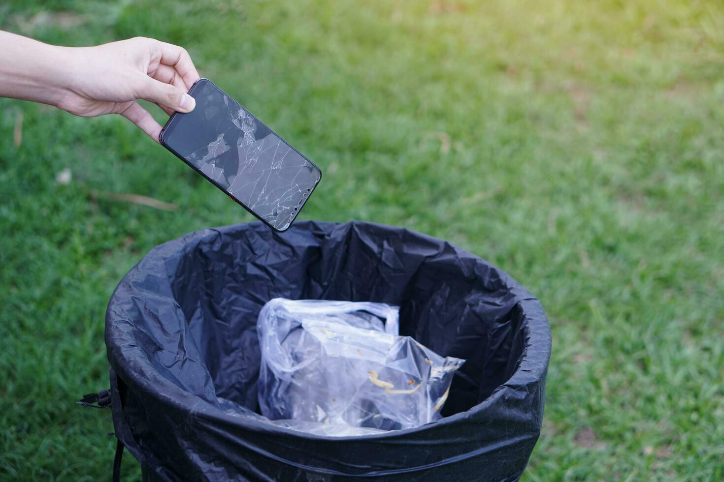 Closeup hand throw broken smartphone into the bin.Concept, hazardous  electronic waste should sort before throwing for safety with environment. Technological  garbage management. photo